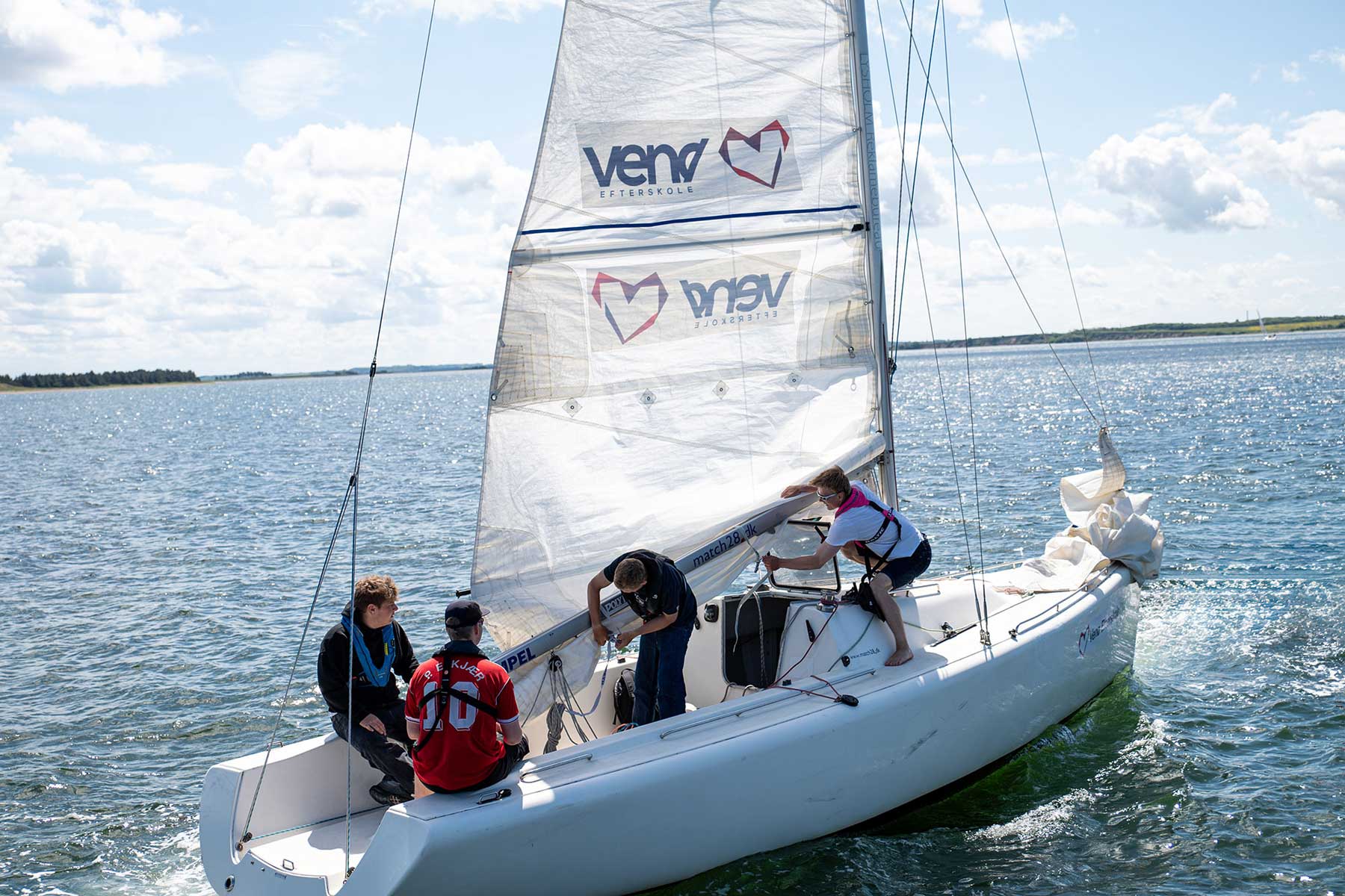 Elever arbejder med sejl og bådhåndtering i en Match 28-sejlbåd på Limfjorden under sejladsundervisningen på Venø Efterskole.