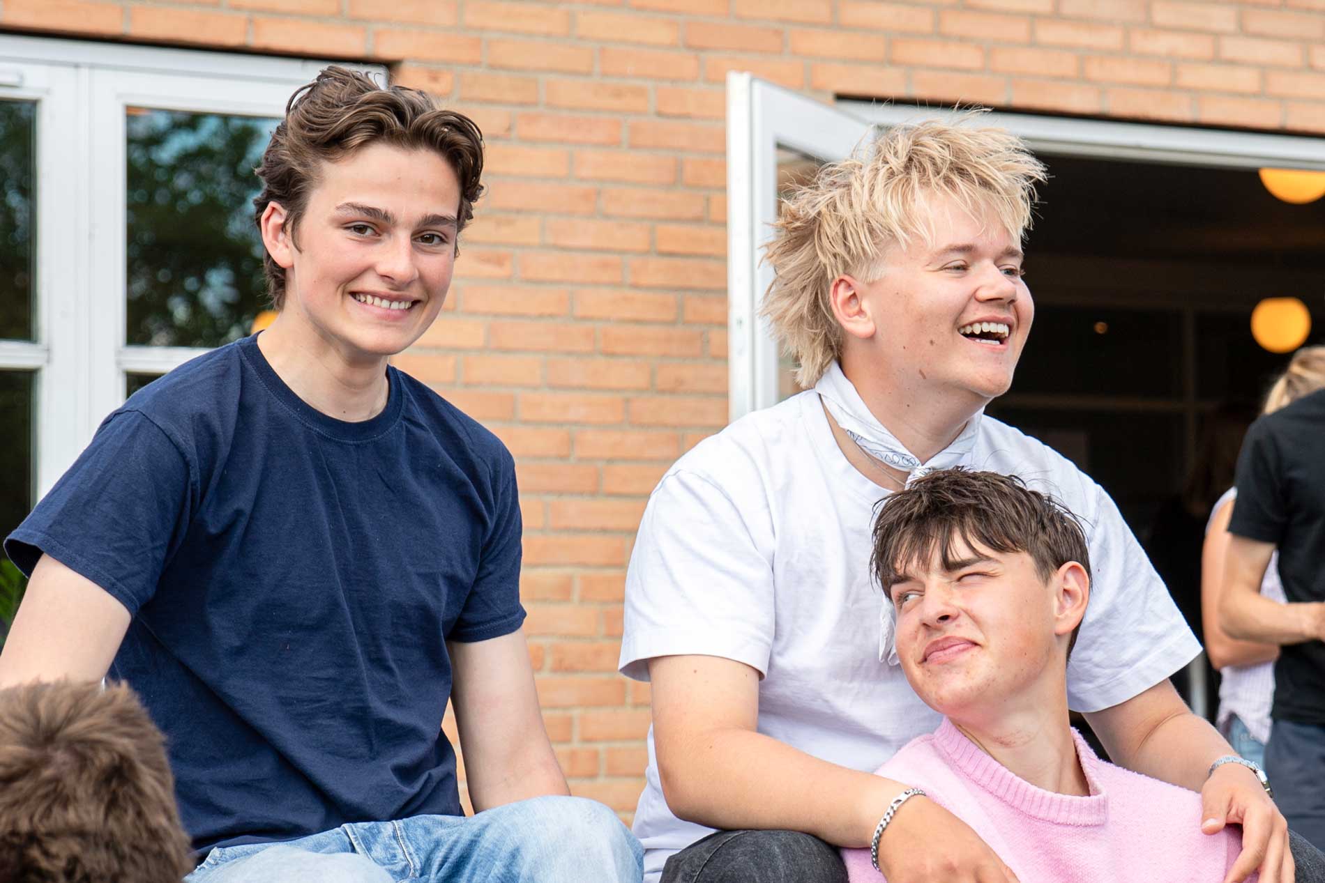 Tre elever griner og hygger sig sammen foran elevbygningen på Venø Efterskole.